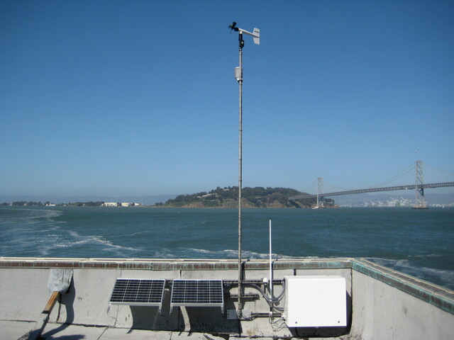 A cluster of meteorological measurement instruments atop a tower overlooking the ocean.